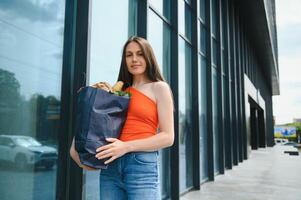 jung Frau Stehen in der Nähe von das Geschäft mit ein Paket von Lebensmittel. foto