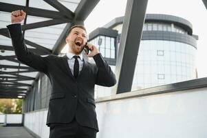 Geschäftsmann lächelnd und erziehen seine Faust im das Luft, mit Büro Gebäude Hintergrund - - Geschäft Erfolg, Leistung, und Sieg Konzepte foto