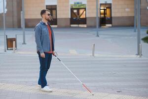 jung gut aussehend blind Mann Gehen mit Stock im Stadt, Dorf foto