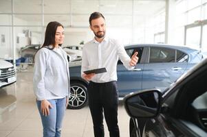 lächelnd Auto Verkäufer Stehen im Auto Salon mit Kunde und zeigen um Autos auf Verkauf foto