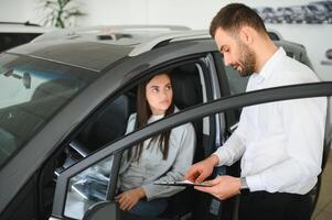 zufrieden glücklich kaukasisch weiblich Klient Kunde Frau Sitzung beim das Rad von Neu Auto während männlich Geschäft Assistent Portion ihr wählen es foto