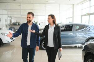 lächelnd Auto Verkäufer Stehen im Auto Salon mit Kunde und zeigen um Autos auf Verkauf foto