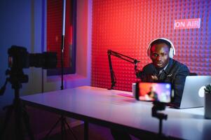 afrikanisch amerikanisch vlogger mit Smartphone zu Film Podcast im Studio. Blogger mit Handy, Mobiltelefon Telefon, Mikrofon und Kopfhörer filmen foto