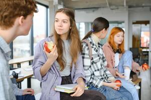 heiter Studenten sind Sitzung beim Schreibtische und Essen ein Apfel während ein brechen foto