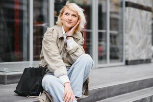 jung schön ziemlich Mädchen Gehen entlang das Straße mit Handtasche und Tasse von Kaffee. foto