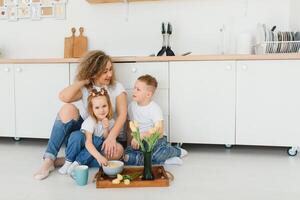 glücklich Mutter umarmen Tochter und Sohn Sitzung auf hölzern Fußboden im modern Küche beim heim. Mama umarmen Kinder. glücklich Familie Beziehung Konzept foto