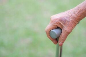 Nahansicht von Hand Senior Frau halten ein Gehen Stock während Stehen im das Garten. Raum zum Text. Gesundheit Pflege Konzept foto