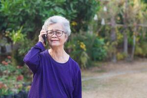 Porträt von Alten Frau reden auf ihr Handy, Mobiltelefon Telefon mit Freude wie seine hört zu zu das Konversation und Stehen im das Garten. Raum zum Text. Konzept von alt Menschen und Technologie foto