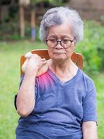 ein Senior Frau haben Schulter Schmerzen Verwendet ein thailändisch Kräuter- komprimieren Ball auf das Schulter. ein alt Frau Wer hat Probleme mit ihr Schulter kann Ursache durch ein Muskel Beanspruchung. Gesundheit Pflege Konzept foto