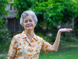 Porträt von ein glücklich Senior Frau zeigen Hände Symbol während Stehen im das Garten. Raum zum Text. Konzept von alt Menschen und Gesundheitswesen foto