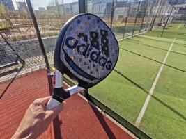 Ukraine Kiew, April 11 2024. Padel Schläger adidas und Padel Ball auf ein Grün Gericht foto