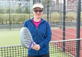 Frau spielen Padel im ein Grün Gras Padel Gericht hinter das Netz foto