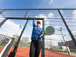 Porträt von positiv jung Frau mit Schläger und Padel Ball auf Tennis Gericht foto