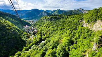 Georgia. Borjomi historisch Park. Aussicht von das Kabel Auto Seilbahn. kann 19, 2024. szenisch Antenne Aussicht von üppig Grün Senke mit Dorf eingebettet unter das Berge unter Himmel mit Wolken. foto