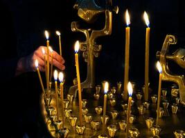 Hand Beleuchtung Kerzen im dunkel Zimmer mit golden Kerze Halter. religiös oder spirituell Zeremonie mit Kerzenlicht. Beleuchtung ein Kerze im ein orthodox oder katholisch Kirche. foto