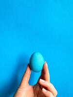 Hand balancieren Blau Ei auf ein Fingerspitze gegen solide Blau Hintergrund, minimalistisch Konzept zum Gleichgewicht, Ostern, und Einfachheit mit Raum zum Text. foto