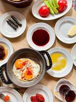 traditionell Türkisch Frühstück mit gebraten Eier im braten Pfanne, geschnitten frisch Tomaten und Gurken, Vielfalt von Marmeladen, Honig, Butter, gerollt Traube Blätter, oben Sicht. gesund Essen Konzept. foto