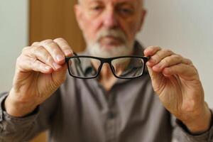 Alten Mann halten Brille im Vorderseite von ihn. schließen hoch. foto