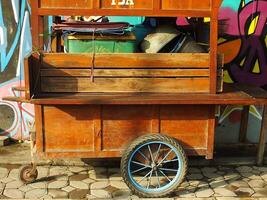 surakarta Stadt, zentral Java, Indonesien. April 11, 2024. ein leeren hausgemacht hölzern Stall Wagen auf das Straße mit bunt Graffiti Kunst Hintergrund. Morgen Ambiente zu Start ein Verkauf Aktivität. foto