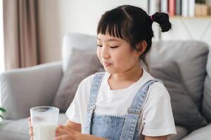 ein jung Mädchen ist Sitzung auf ein Couch und Trinken Milch foto