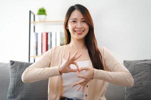 ein jung taub Frau ist Sitzung auf ein Couch und Herstellung ein Zeichen Sprache zu kommunizieren. foto