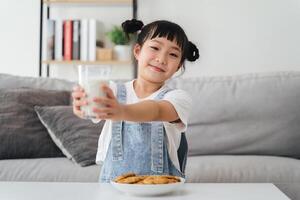 ein jung Mädchen ist halten ein Glas von Milch und ein Teller von Kekse foto