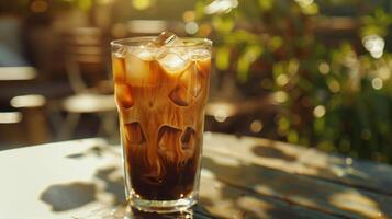 vereist Kaffee, Nahaufnahme, mit Kaffee Eis Würfel und ein Spritzen von Mandel Milch, im ein hoch Glas, auf ein sonnig draussen Tisch. foto