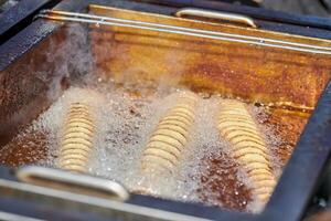 Kochspirale Bratkartoffel in siedendem Öl, fett- und kalorienreiches Fastfood, ungesund lecker foto