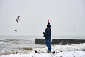 Alter Mann, der im Winter Vögel auf See füttert foto