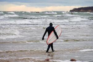 männlicher surfer im badeanzug, der mit surfbrett am meer entlang geht foto