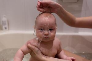 schön gemischt Rennen Baby Baden im das Badewanne. Nahansicht Schuss, Wasser Gießen auf das Gesicht foto