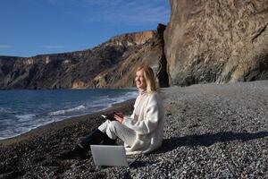 jung schön Frau Arbeiten auf ein Laptop Sitzung auf das Strand foto