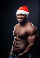 gut aussehend attraktiv passen Santa auf dunkel Hintergrund. mit nacktem Oberkörper muskulös Mann mit komisch Weihnachten Hut. foto