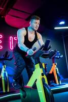 muskulös aktiv Mann im Sportbekleidung Ausbildung Cardio mit Fahrrad. gut aussehend stark Mann Radfahren im Fitnessstudio. foto