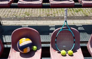 ein Tennis Schläger, Bälle und ein Volleyball auf ein Bank auf das Sport Tribun foto