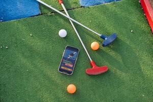 Golf Ausrüstung auf das Grün Rasen. Mini Golf Sport Wetten auf ein Smartphone foto