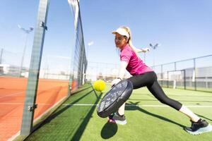 aktiv jung Frau versuchen zu schlagen das Ball durch Padel Schläger während spielen Tennis im das Gericht foto