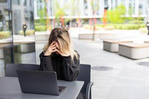 müde jung Geschäft Frau im schwarz passen mit Kopfhörer ist Sitzung mit Augen geschlossen im Vorderseite von Laptop foto