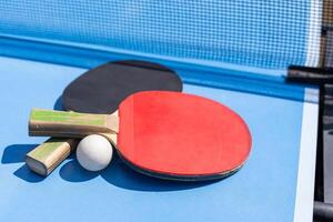 rot und schwarz Tabelle Tennis Paddel und Ball auf das Blau Tabelle Tennis Tabelle mit Netz. Klingeln Pong Konzept mit Kopieren Raum foto