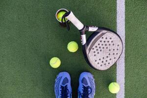 Gelb Bälle auf Gras Rasen in der Nähe von Padel Tennis Schläger hinter Netz im Grün Gericht draußen mit natürlich Beleuchtung. Paddel ist ein Schläger Spiel. Fachmann Sport Konzept mit Kopieren Raum. foto