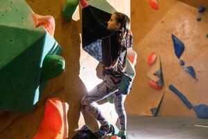 süß wenig Mädchen Klettern auf künstlich Felsbrocken Mauer im Fitnessstudio foto