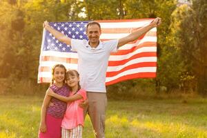 glücklich Familie mit das Flagge von Amerika USA beim Sonnenuntergang draußen foto
