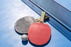 rot und schwarz Tabelle Tennis Paddel und Ball auf das Blau Tabelle Tennis Tabelle mit Netz. Klingeln Pong Konzept mit Kopieren Raum foto