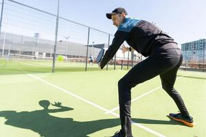 ein Padel Spieler springen zu das Ball, gut suchen zum Beiträge und Poster. Mann mit schwarz Schläger spielen ein Spiel im das öffnen hinter das Netz Gericht draußen. Fachmann Sport Konzept mit Raum zum Text foto