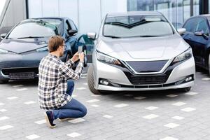 Mann Kunde nehmen Foto zu Handy, Mobiltelefon Telefon wählt Auto und will zu Kaufen Neu Auto im Ausstellungsraum