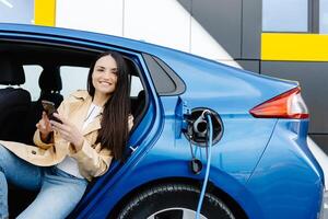 Geschäft Dame Sitzung Innerhalb Laden elektrisch Auto und mit modern Smartphone. Technologie und Transport Konzept. foto