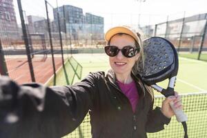 sportlich europäisch Frau Padel Tennis Spieler Züge auf das draussen Gericht mit ein Schläger zu schlagen das Ball foto