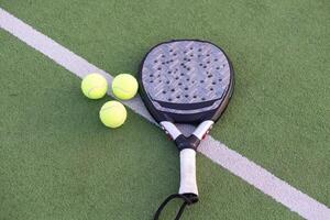 Gelb Bälle auf Gras Rasen in der Nähe von Padel Tennis Schläger hinter Netz im Grün Gericht draußen mit natürlich Beleuchtung. Paddel ist ein Schläger Spiel. Fachmann Sport Konzept mit Kopieren Raum. foto