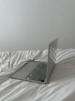 Laptop auf Weiß Bett Blätter im ein minimalistisch Schlafzimmer foto
