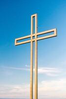 golden Kreuz gegen ein Hintergrund von Blau Himmel mit Wolken. ein minimalistisch Aussicht von ein goldfarben Kreuz gegen das Himmel. foto